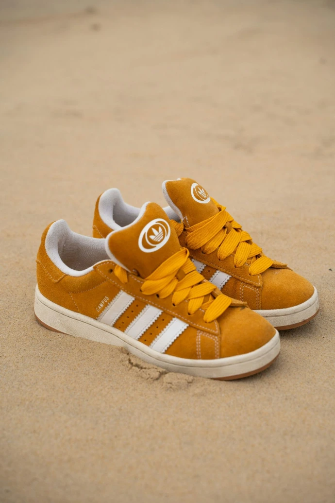 Pair of mustard yellow adidas sneakers on sand.